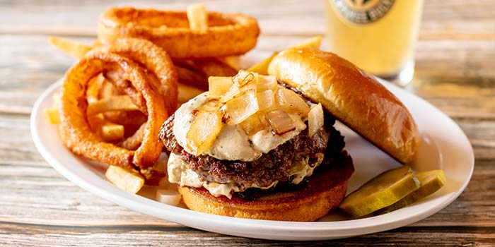 Warm burger topped with cheese and caramelized onions, served with pickles and onion rings at Rapids Riverside Bar & Grill in South Range WI.