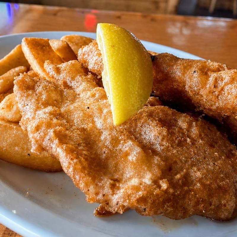 Enjoy a Rapids Riverside Friday Fish Fry: golden fried fish, thick-cut fries, and a lemon wedge.